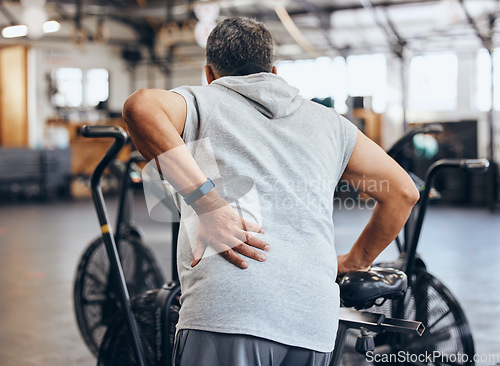 Image of Sports, gym and injury, old man with back pain, emergency during workout at fitness studio. Health, wellness and inflammation, senior person with hand on muscle cramps while training on exercise bike