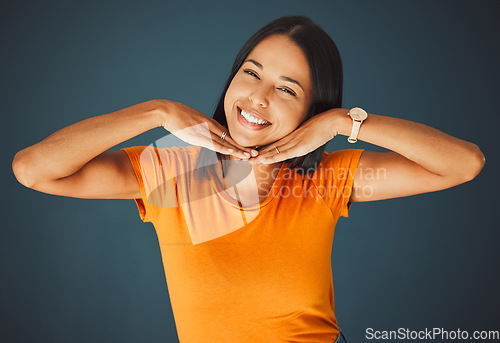 Image of Woman, hands on face and smile portrait in studio for kindness, beauty and motivation for happiness. Model person with orange t-shirt for fashion, happy mindset and mental health on a blue background