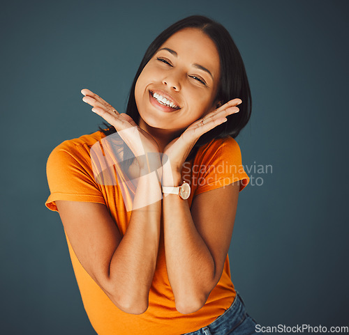 Image of Woman, happy and hands on face portrait in studio for smile, beauty and motivation for happiness. Model person with orange t-shirt for fashion, positive mindset and mental health on a blue background