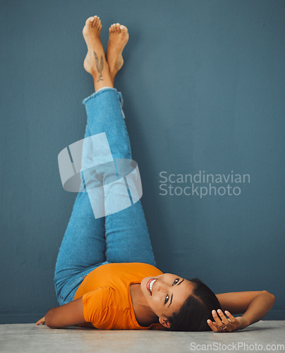 Image of Woman on floor, smile on face with legs up on wall background and creative pose in studio. Teal copy space, young model laying on ground, portrait of happy person alone and body relaxing aesthetic