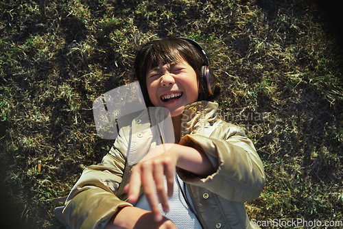 Image of Headphones, nature and Asian child on the grass to relax, chill and listen to music with freedom. Happy, smile and excited girl kid streaming a podcast or the radio in outdoor field, park or garden.