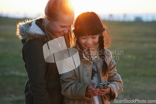 Image of Phone, kids and friends at park on social media, internet browsing or web scrolling. Technology, smartphone and happy children or girls with mobile for texting, streaming or gaming outdoors at sunset