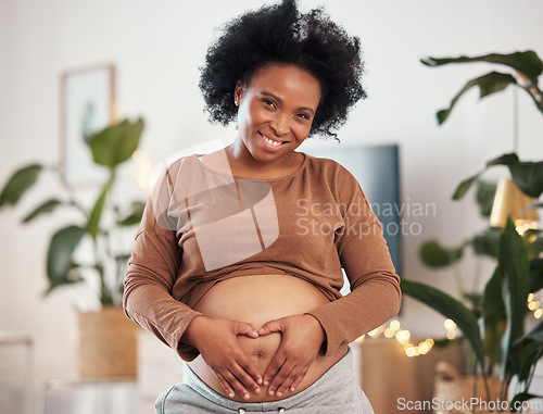 Image of Pregnant mother, heart hands on belly and portrait of happy black woman alone in Jamaica living room. Excited future parent, holding healthy abdomen at home and natural beauty in pregnancy care