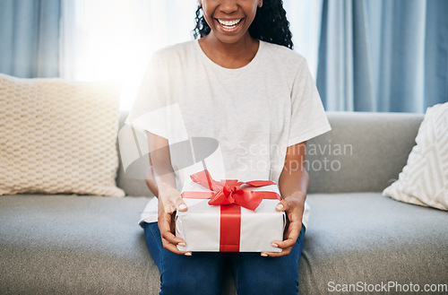 Image of Present, box and woman on a sofa in the living room with a giving gesture for celebration or event. Bow, wrapping paper and African female with a present for christmas, birthday or holidays in house.