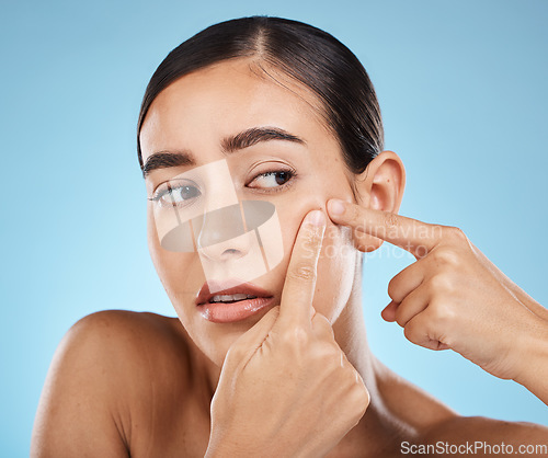 Image of Woman, face and pop pimple with hands and acne, anxiety and stress, beauty and skincare isolated on blue background. Skin problem, facial and cosmetics, dermatology and cosmetic care in studio