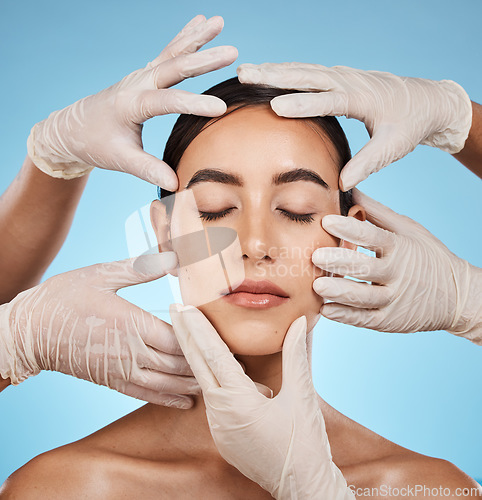 Image of Plastic surgery, beauty and hands on the face of a woman isolated on a blue background in a studio. Feeling, skincare and doctors touching a model for a botox, cosmetics or dermatology consultation