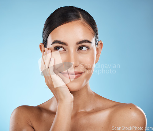 Image of Woman is thinking, face and happy with beauty, natural cosmetics and glow isolated against blue background. Clean, cosmetic care and hand with facial, makeup and healthy skin with skincare in studio