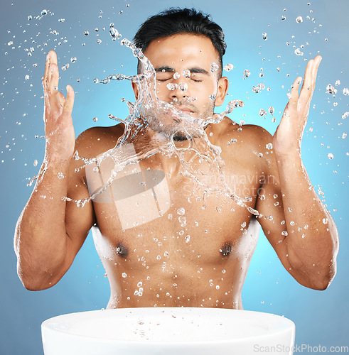 Image of Water splash, facial and man in studio for skincare, wellness and grooming on blue background. Cleaning, beauty and moisture by Mexican model relax with luxury, routine and face treatment isolated