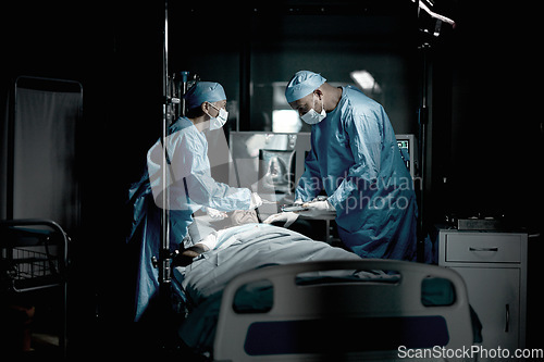 Image of Surgery, doctors and surgeon in medical theatre for teamwork, expert services or emergency in dark room. Doctors saving patient life on table in hospital theater for healthcare, insurance and support