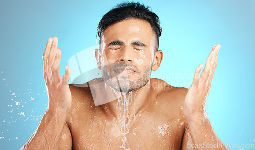 Image of Water splash, face and man in studio for skincare, wellness and grooming on blue background. Cleaning, beauty and facial by Mexican model relax with luxury, routine and moisture while isolated