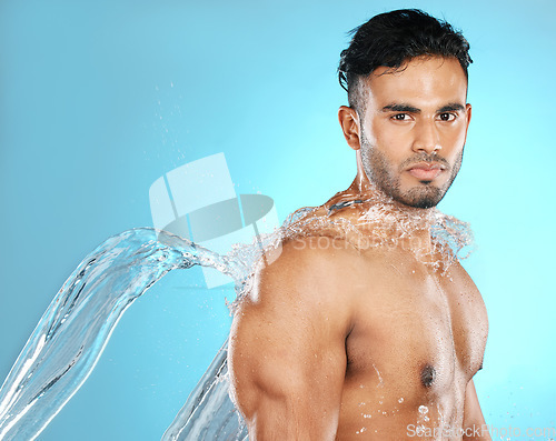 Image of Water splash, portrait and man for beauty, skin and skincare cleaning his body, muscle and topless. Mexican, strong and serious model with moisture, cleanse and hydration in studio blue background