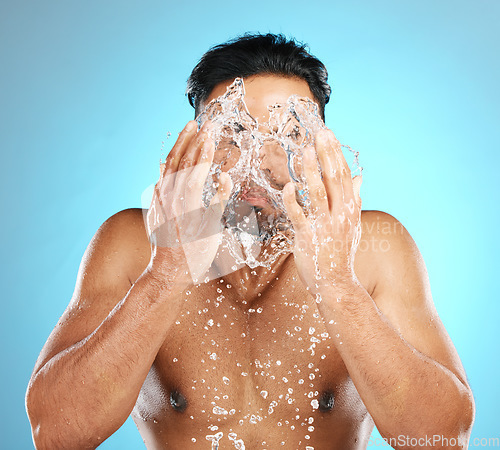 Image of Man, face and water splash in studio with skincare, wellness and grooming on blue background. Cleaning, beauty and moisture by Mexican model relax with luxury, routine and facial while isolated