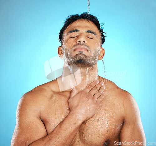 Image of Water, shower and man cleaning skin, beauty and skincare for his body, muscle and topless. Latino, male and wellness model with moisture, cleanse and hydration isolated in studio blue background