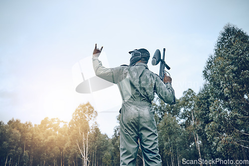 Image of Paintball, rock hand sign or man in a shooting game playing on a fun battlefield with pride. Success, war winner or soldier with weapon or gun for in celebration of winning survival competition