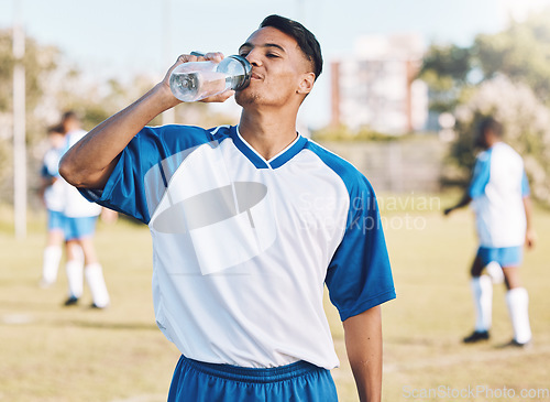 Image of Drinking water, break and soccer player on a sports field resting after match or competition on a sunny day. Man, athlete and sportsman refreshing during a game happy and smiling for due to fitness