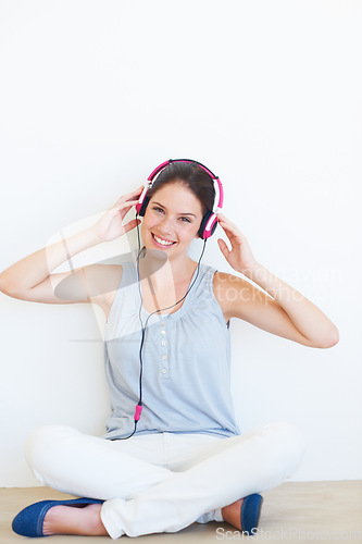 Image of Portrait, music and woman on a floor with headphones in studio, happy and streaming on a wall background. Face, smile and girl relax with podcast, radio or audio track while sitting against mockup