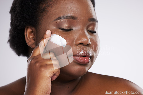 Image of Face, skincare and cream with a model black woman in studio on a gray background for plus size beauty. Eyes closed, skin and lotion with an attractive young female indoor to apply facial treatment