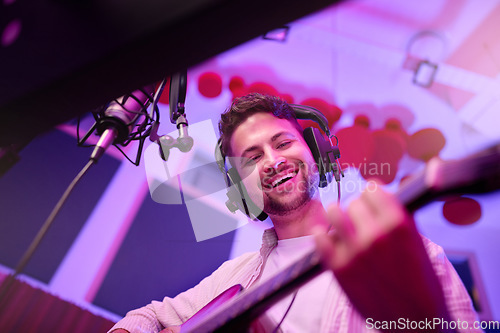 Image of Happy man, musician or guitar in neon studio, recording production or performance for radio, label or low angle concert. Guitarist, artist or singer playing strings instrument on headphones practice