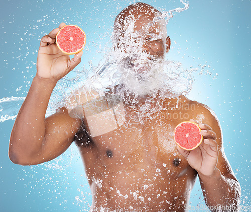 Image of Black man, water splash and fruit for skincare, grapefruit or vitamin C and hydration against a blue studio background. Happy African American male smiling and holding food for health and wellness