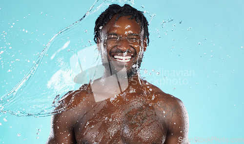 Image of Water splash, beauty and black man isolated on blue background for face cleaning, body shower and skincare. Strong, muscle and happy model or person facial glow in studio headshot washing or hygiene