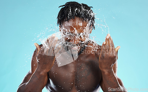 Image of Water, splash and cleaning with a model black man in studio on a blue background for hydration or hygiene. Bathroom, skincare or wellness with a young male wahsing his face for natural skin treatment