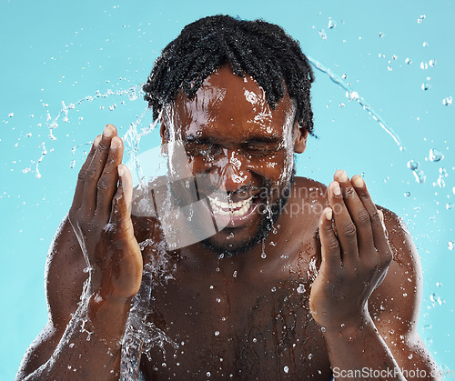 Image of Water splash, cleaning and face with a model black man in studio on a blue background for hydration. Bathroom, skincare and hygiene with a young male washing his face for natural skin treatment