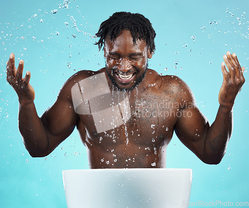 Image of Water splash, cleaning and hydration with a model black man in studio on a blue background for hygiene. Bathroom, skincare and wellness with a young male washing his face for natural skin treatment