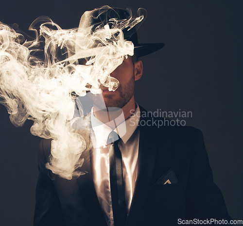 Image of Mafia, criminal and man with smoke in a suit for fashion isolated on a dark background in a studio. Sexy, vintage and businessman looking stylish, gangster and rich while smoking on a backdrop