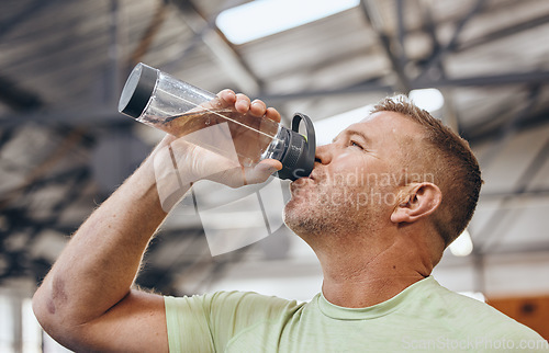 Image of Man, fitness and drinking water bottle for detox after workout, exercise or cardio training indoors. Sporty male with drink in hydration or healthy endurance, recovery or thirst for sports exercising