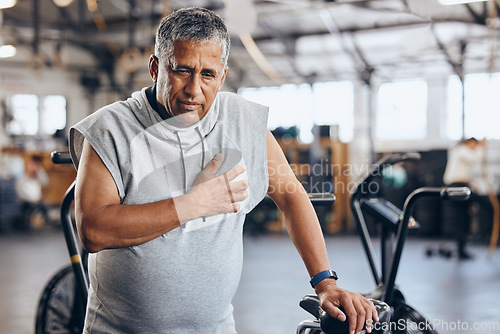 Image of Gym, pain in chest and senior man with medical emergency during sports workout at fitness studio. Health, wellness and inflammation, old man with hand on heart attack while training on exercise bike.