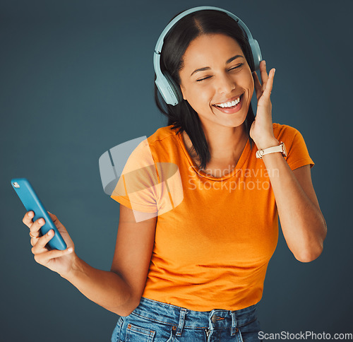 Image of Music, headphones and woman streaming a song on phone or mobile app isolated against a studio background. Fun, sound and female enjoying and listening to podcast, radio or audio smiling and happy