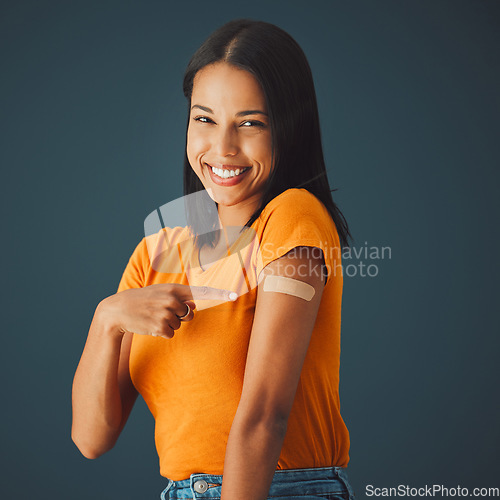 Image of Black woman, portrait and covid plaster in studio for vaccine, safety or wellness by blue background. Happy gen z girl, fashion and pointing for healthcare, medicine or lifestyle choice to stop virus
