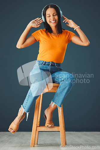 Image of Woman, headphones and listening to music while dancing and streaming online on a studio background. Happy gen z person with headset for podcast, radio or audio sound on chair to relax for freedom