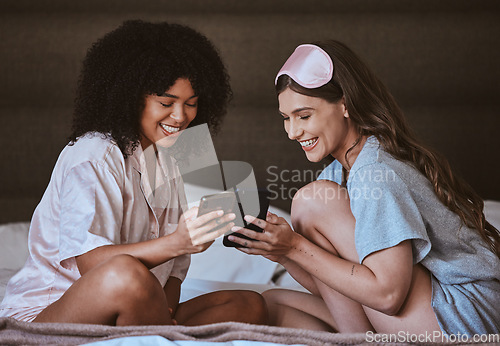 Image of Woman, friends and phone on bed with smile for social media, networking or funny meme in sleepover at home. Happy women smiling, laughing or relaxing with smartphone entertainment in the bedroom