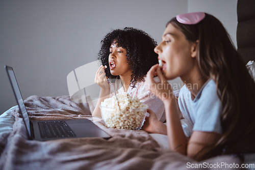 Image of Laptop, movie and relax with friends and popcorn in bedroom for sleepover, bonding and streaming. Technology, internet and online with women at night for cinema, subscription and film entertainment