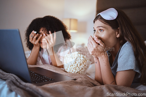 Image of Laptop, movie and horror with friends and popcorn in bedroom for sleepover, bonding and streaming. Technology, internet and relax with shocked women at night for cinema, subscription or entertainment