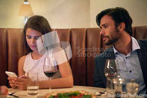 Image of Phone, chatting and couple on a date at a restaurant for valentines day, romance or anniversary. Communication, upset and annoyed man watching his girlfriend sitting on her cellphone at dinner.