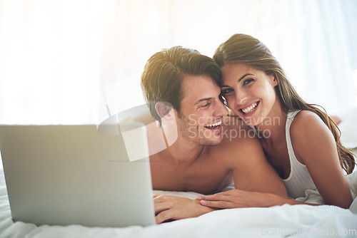 Image of Laptop, happy and couple lying in bed together while watching a online movie or video at their home. Happiness, smile and portrait of a woman browsing the internet on computer with husband in bedroom