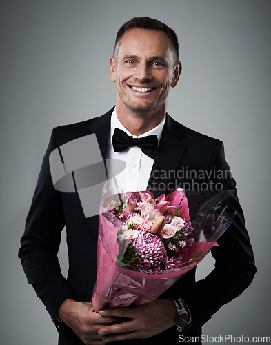 Image of Portrait, man and bouquet of flowers, suit and happiness for Valentines day, romance and on grey studio background. Face, male and guy with floral gift, smile and gesture for love, romantic and happy