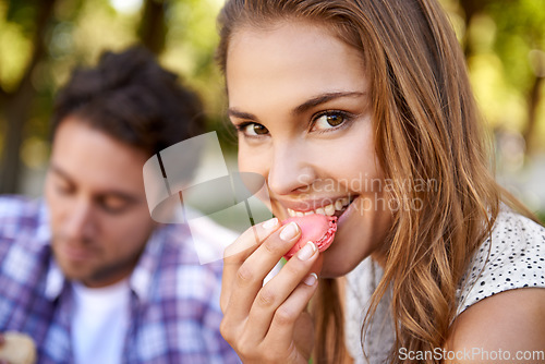 Image of Couple picnic, woman eating candy and portrait on grass with happiness, kindness and love on valentines date. Girl, macaroon and man together at nature park with food for bonding, romance and care