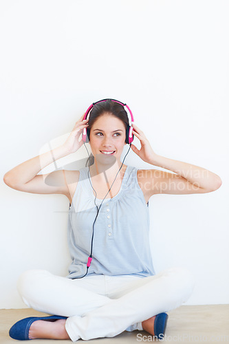 Image of Music, thinking and woman on a floor with headphones in studio, happy and streaming on a wall background. Contemplation, smile and girl relax for podcast, radio or audio track while sitting on mockup