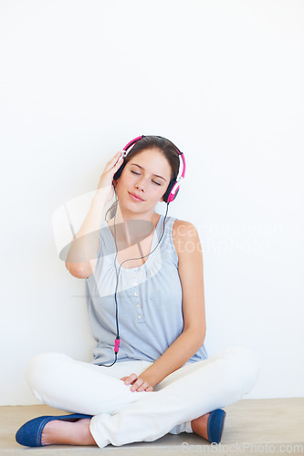 Image of Relax, music and woman on a floor with headphones in studio, happy and streaming on a wall background. Zen, feeling and girl with wellness podcast, radio or audio track while sitting against mockup