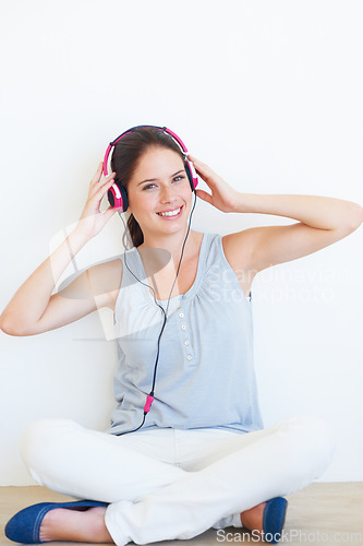 Image of Music, portrait and woman on a floor with headphones in studio, happy and streaming on a wall background. Face, smile and girl relax with podcast, radio or audio track while sitting against mockup