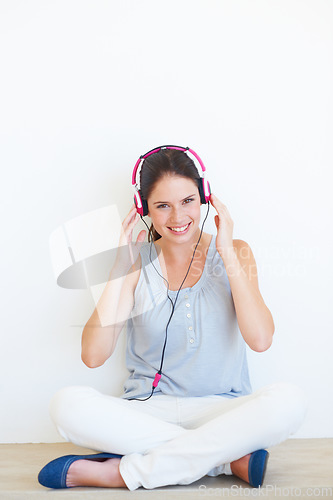 Image of Portrait, woman and music on a floor with headphones in studio, happy and streaming on a wall background. Face, smile and girl relax with podcast, radio or audio track while sitting against mockup