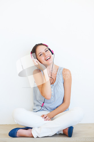 Image of Headphones, music and portrait of woman on a floor in studio, happy and streaming on a wall background. Face, smile and girl relax with podcast, radio or audio track while sitting against mockup