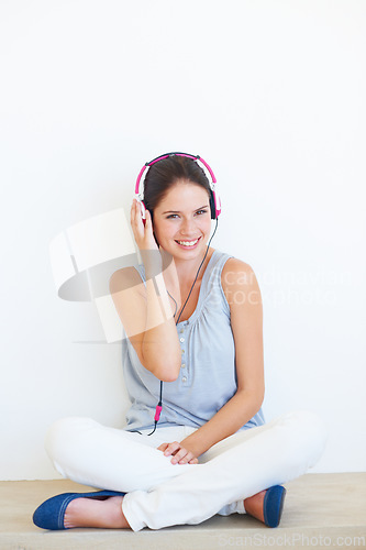 Image of Woman, music and portrait with headphones on a floor in studio, happy and streaming on a wall background. Face, smile and girl relax with podcast, radio or audio track while sitting against mockup