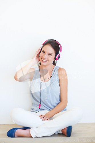 Image of Music, portrait and headphones for woman on a floor in studio, happy and streaming on a wall background. Face, smile and girl relax with podcast, radio or audio track while sitting against mockup