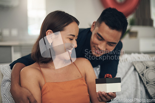 Image of Love, surprise and man giving his wife a gift for valentines day, anniversary or romantic event. Happy, smile and husband giving his woman a present while relaxing on the sofa in living room at home.