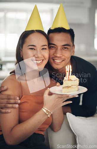 Image of Portrait, birthday and cake with a couple in their home, holding dessert for celebration in party hats. Love, candle or romance with a young man and woman celebrating together in their house