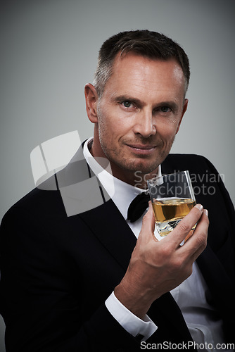 Image of Portrait, whiskey and elegant with a man model in studio on a gray background drinking an alcoholic beverage. Gentleman, whisky and tuxedo with a handsome mature man enjoying a drink of alcohol